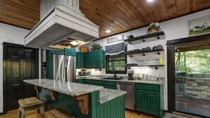 A kitchen with green cabinets, a stainless steel refrigerator, and a wooden island with stools. - Holly Hill Secluded Retreat 7 acrs, Perfect 2 Bedroom, Hot Tub, Pets (Broken Bow)
