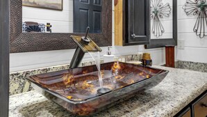 A modern bathroom with a glass vessel sink, a black door, and a decorative metal wall piece. - Holly Hill Secluded Retreat 7 acrs, Perfect 2 Bedroom, Hot Tub, Pets (Broken Bow)