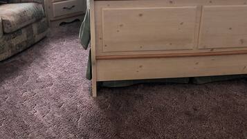 Un dormitorio con una cama de madera, una mesita de noche con lámpara, un sillón estampado y una ventana con cortinas.