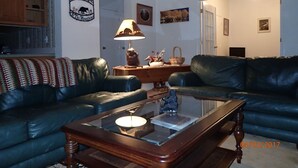 A living room with two black leather sofas, a wooden coffee table, a lamp, and a wall sign that reads "Welcome to The Mountains."