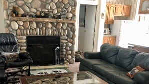 A living room with a stone fireplace, a leather armchair, a green sofa, and a coffee table.
