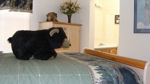 A bed with a patterned bedspread, a dresser with a vase of flowers, and a framed picture on the wall.