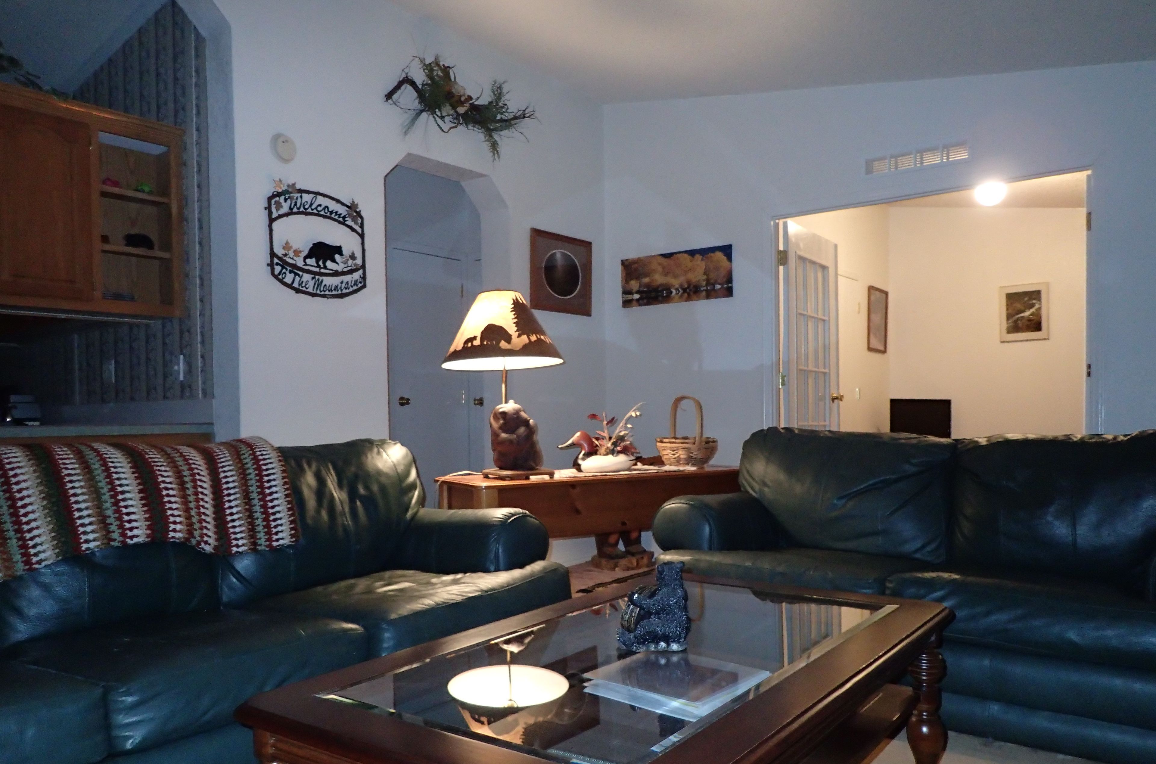 Un salon avec deux canapés en cuir noir, une table basse en bois, une lampe et un panneau mural sur lequel on peut lire : « Bienvenue à la montagne ».