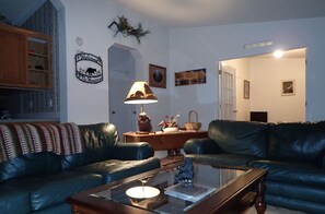 A living room with two black leather sofas, a wooden coffee table, a lamp, and a wall sign that reads "Welcome to The Mountains." - Escape to Black Bear Hollow~Secluded in a Beautiful Aspen Grove! (Red Feather Lakes)