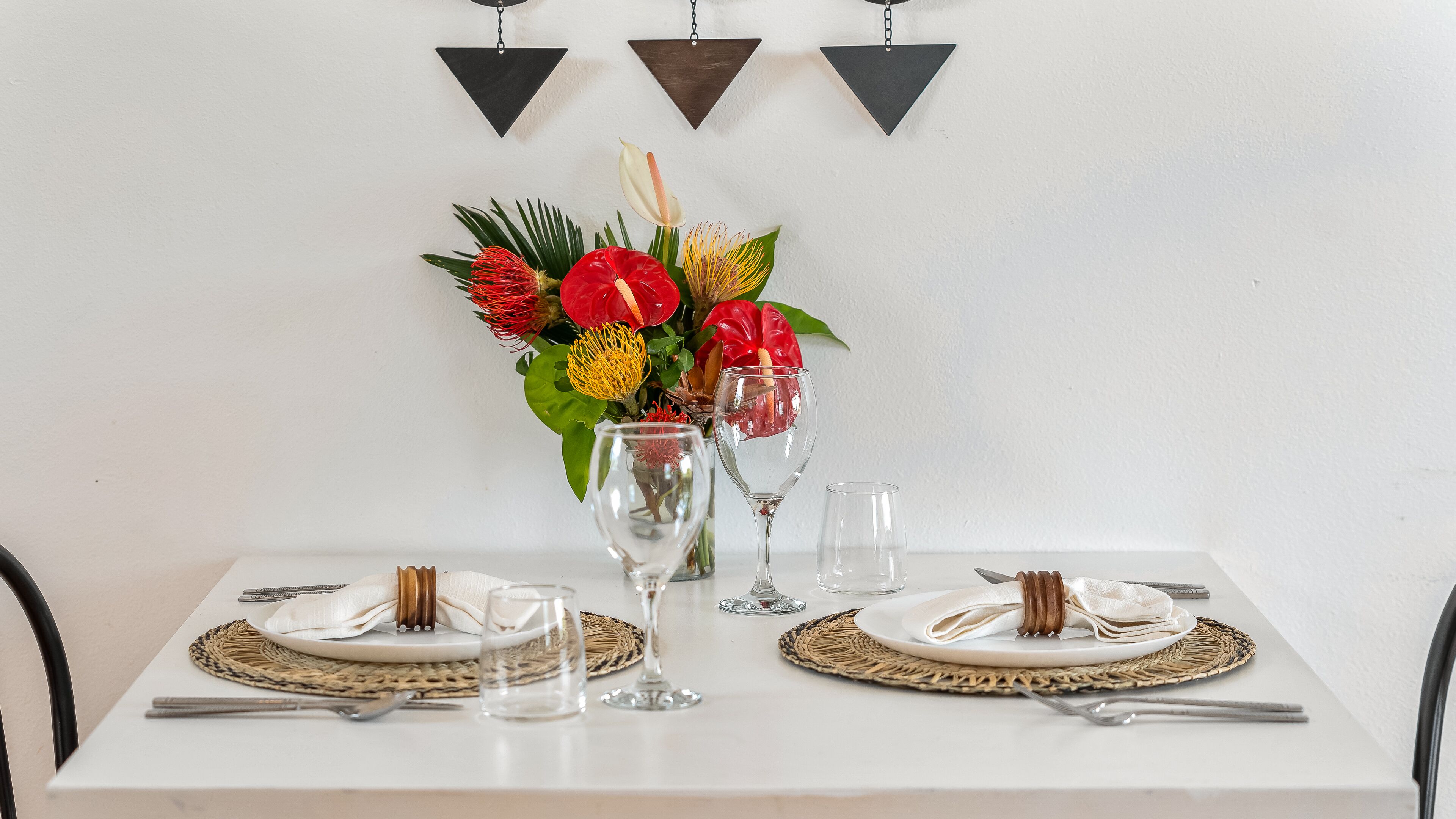 Une table à manger dressée avec des assiettes, des couverts et des verres, agrémentée d’un centre de table composé de fleurs et d’un vase.