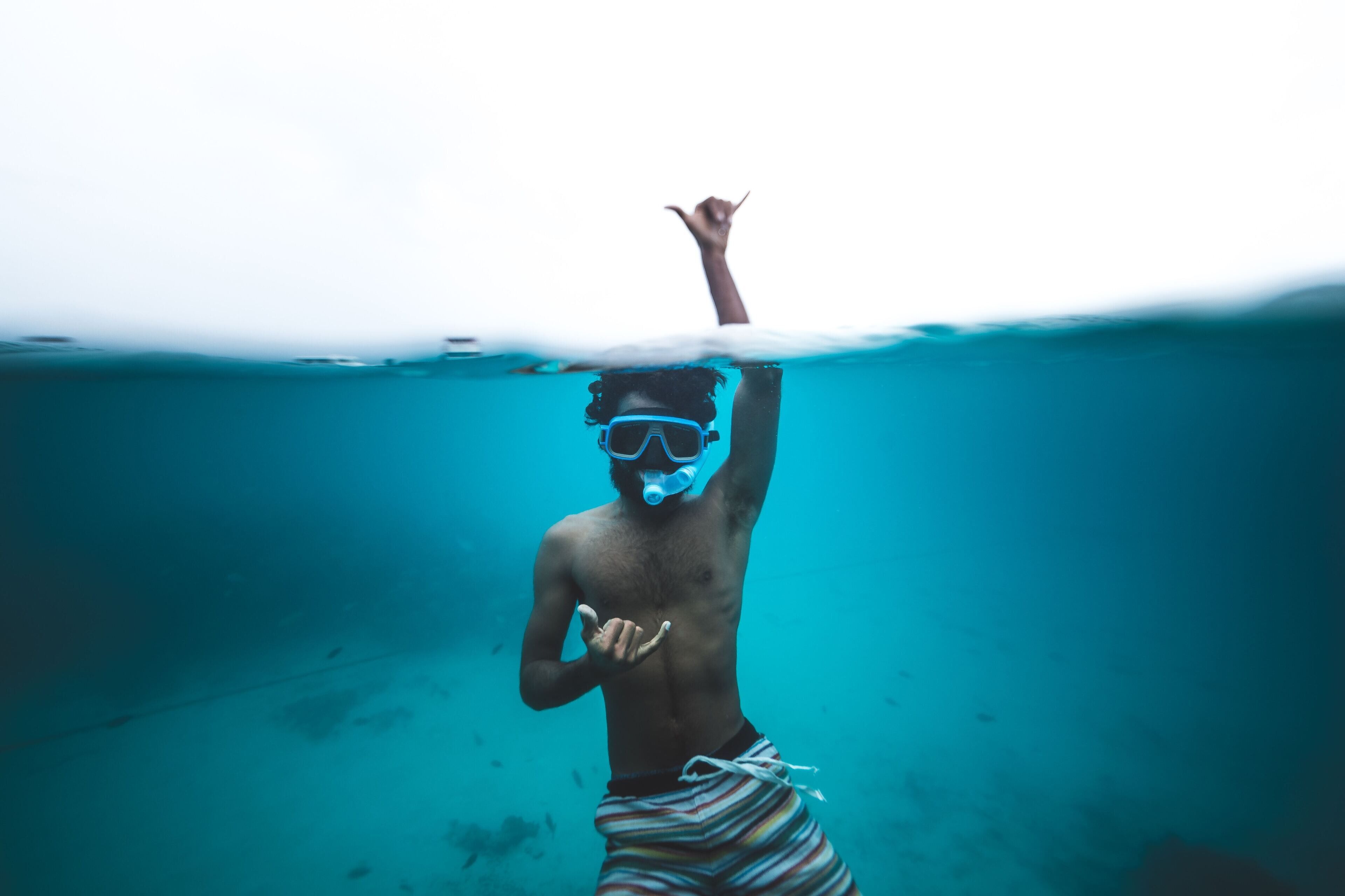 Une personne sous l’eau, tenant une planche de surf, portant un maillot de bain rayé et un masque de plongée.