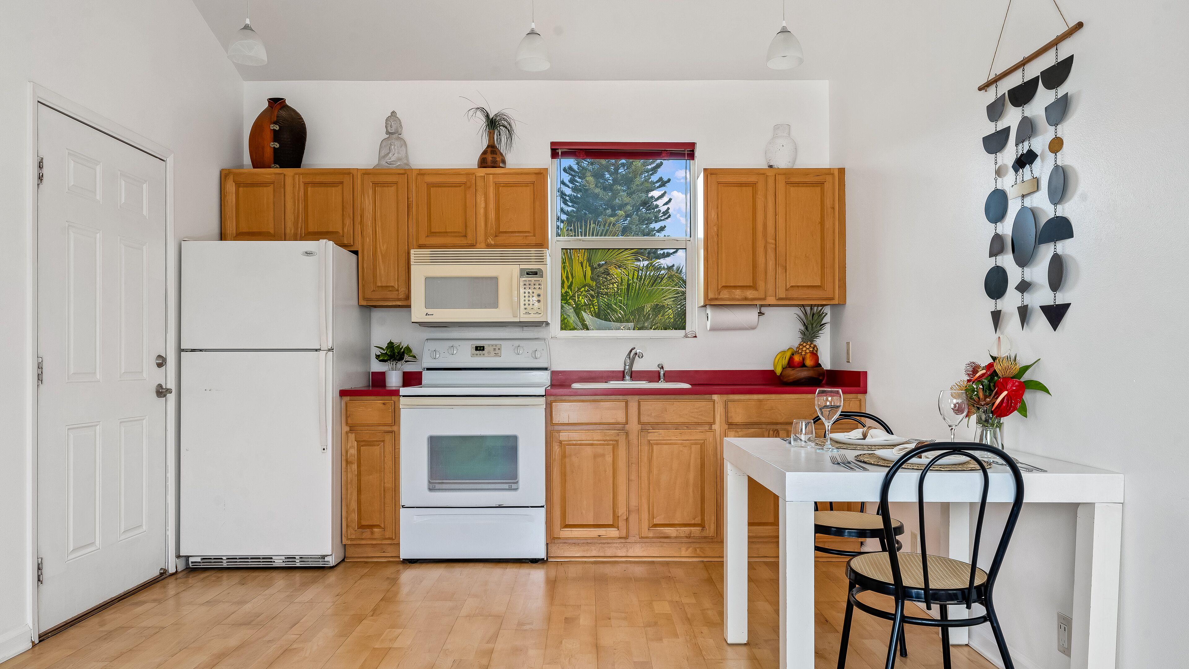 Una cocina compacta con armarios de madera, un refrigerador blanco, un microondas y una estufa. Hay una ventana con vista a árboles y un comedor con mesa y sillas.