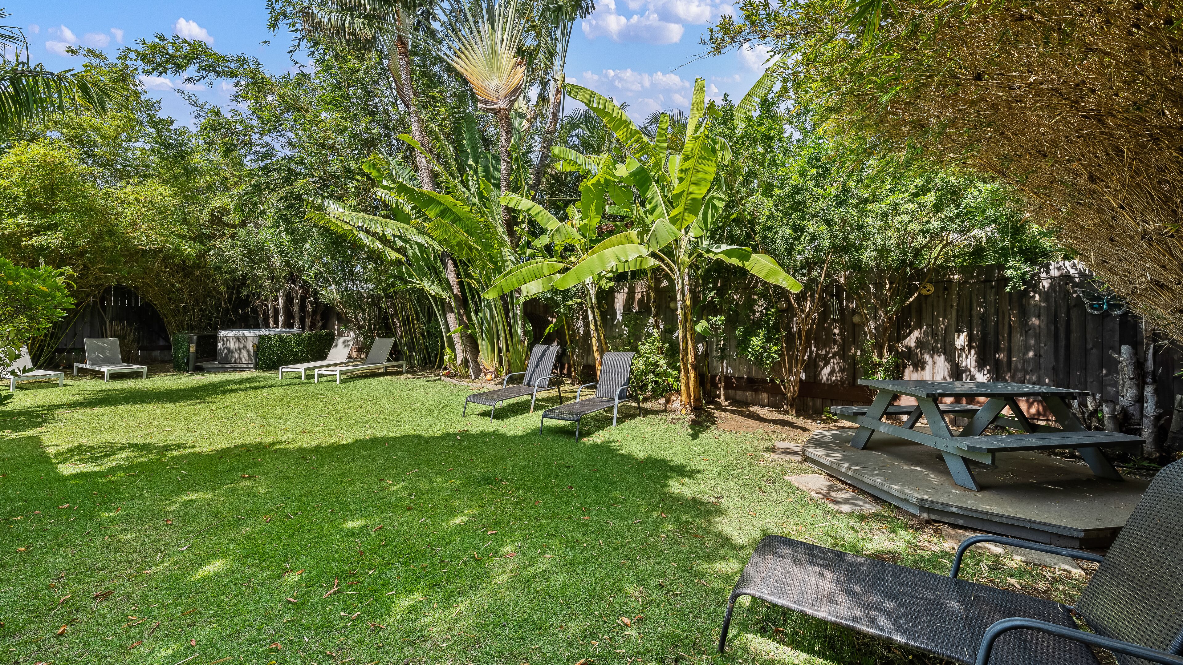 A backyard with a grassy lawn, a wooden deck, and a picnic table.
