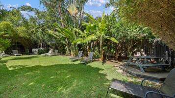 A backyard with a grassy lawn, a wooden deck, and a picnic table.