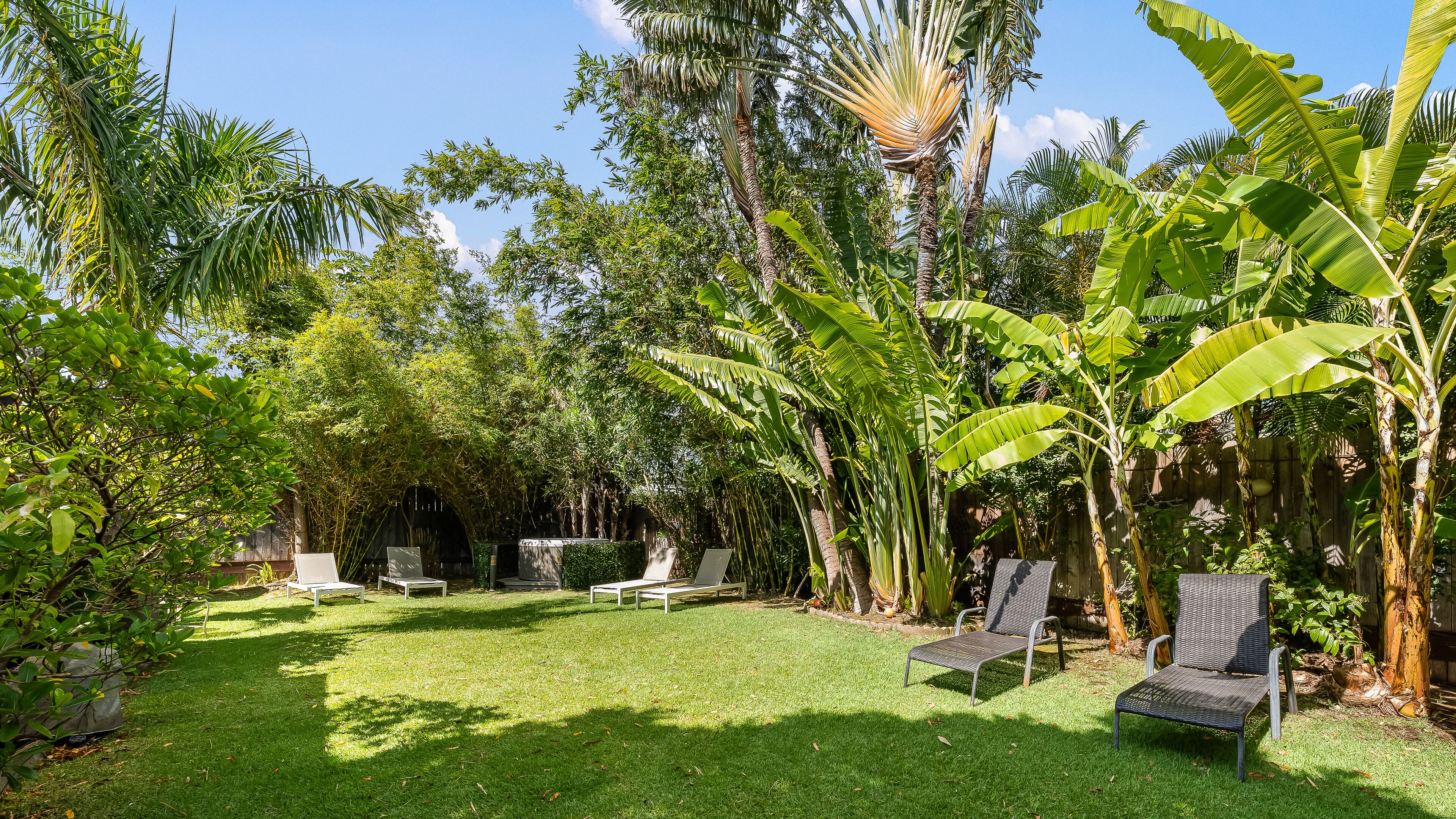 Un jardin luxuriant avec une pelouse verdoyante, plusieurs bancs en bois et de grands bananiers.