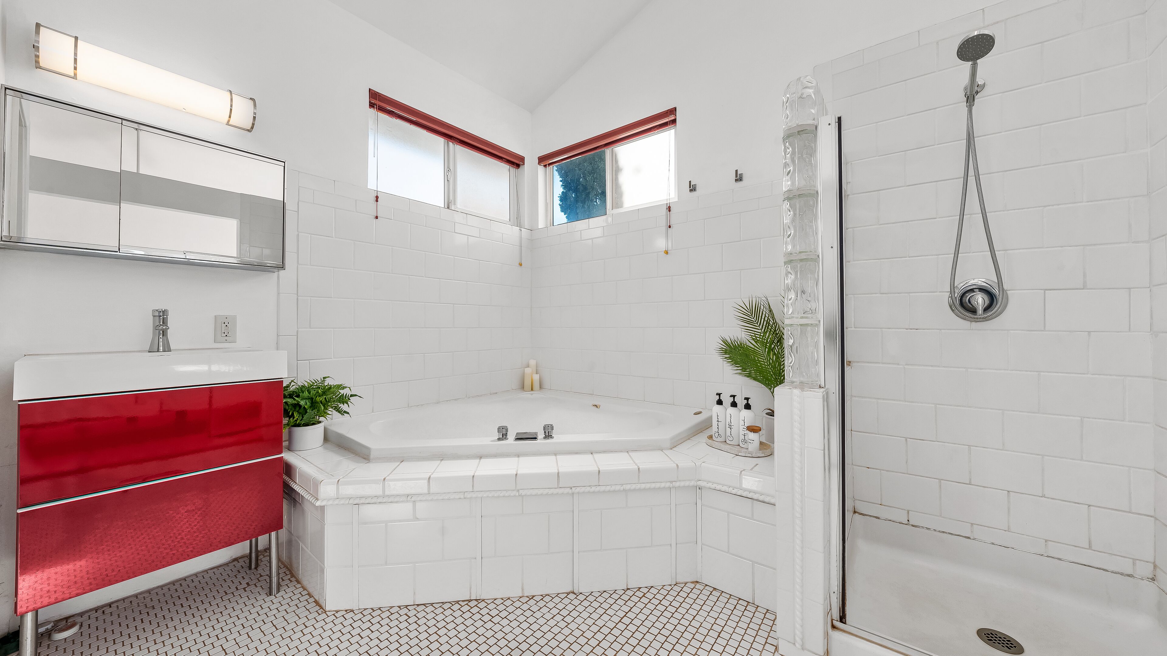 Une salle de bain moderne avec une douche carrelée de carreaux blancs, un meuble-lavabo rouge et un grand miroir.