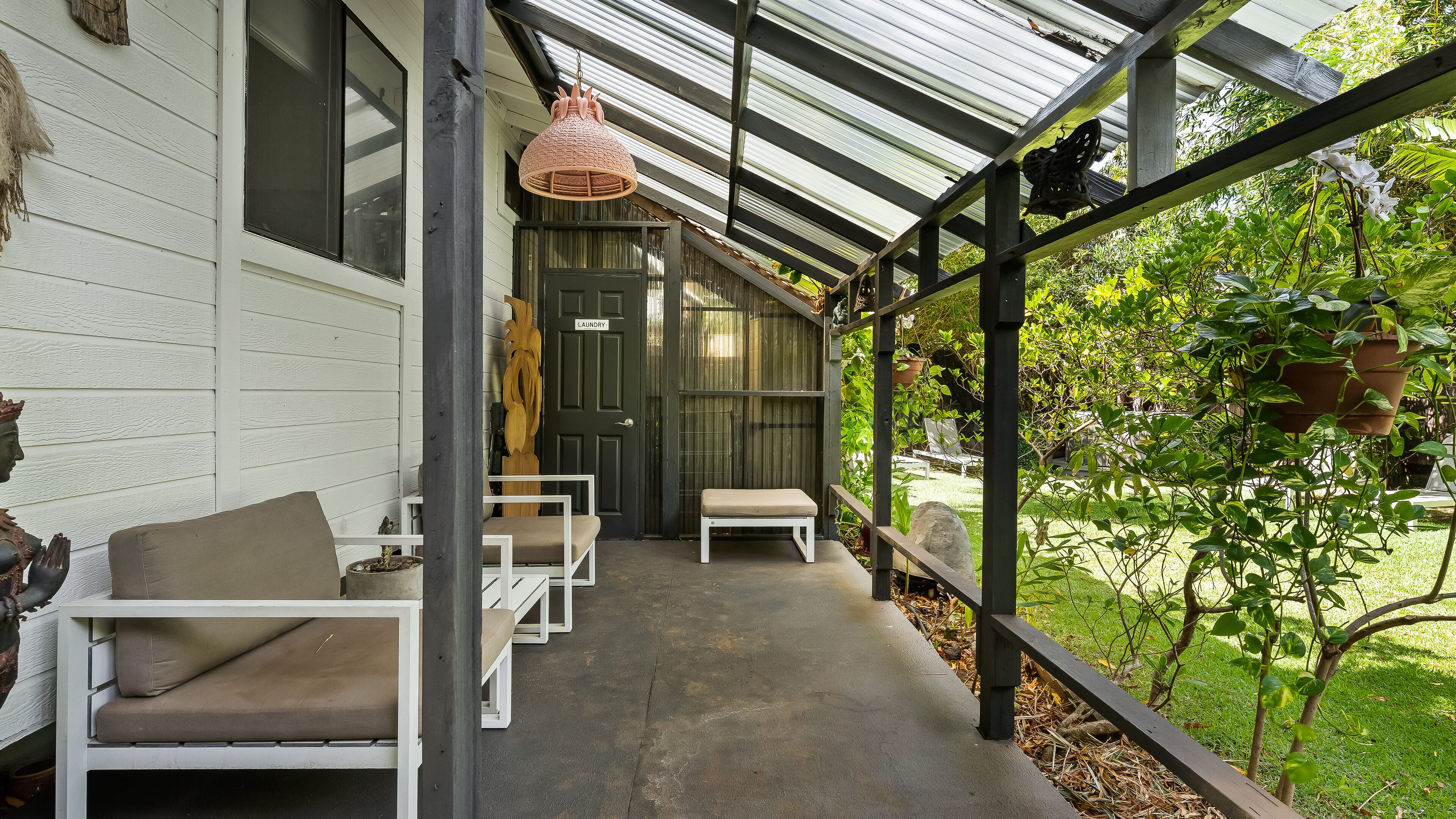 A covered porch with white furniture, a hanging light fixture, and a view of a garden.