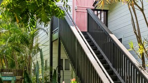 Un escalier menant à un bâtiment dont la porte est rose, le tout entouré de verdure.