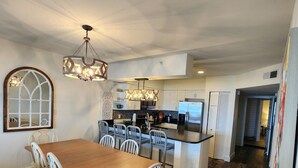 Ett modernt kök med en central köksö, vita köksskåp och en matplats med ett träbord och vita stolar.