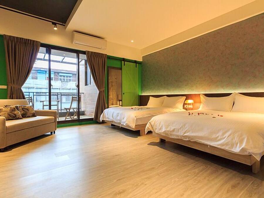A modern hotel room with two beds, a sofa, and a large window.