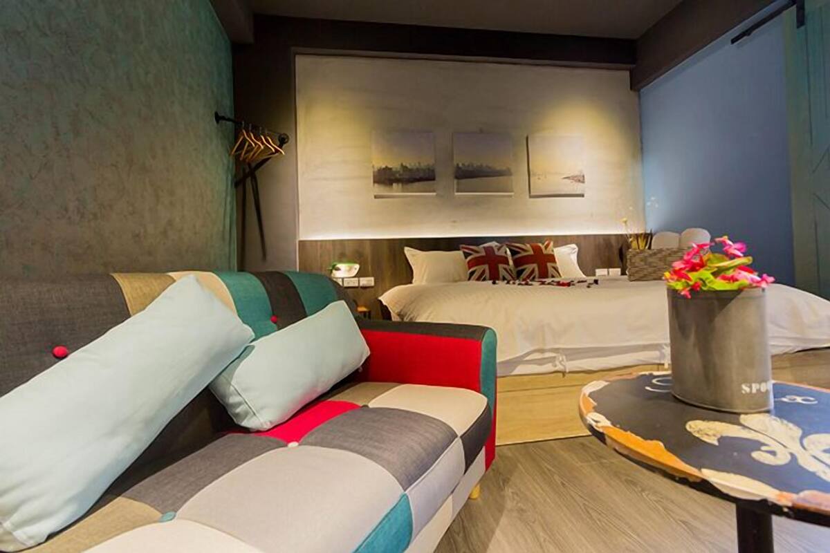 Un dormitorio moderno con un sofá, una cama y una pequeña mesa con un jarrón de flores.