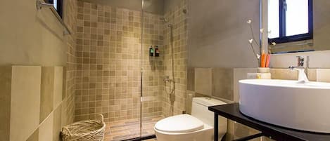 Un baño moderno con cabina de ducha de vidrio, inodoro blanco y un lavamanos grande con espejo superior.