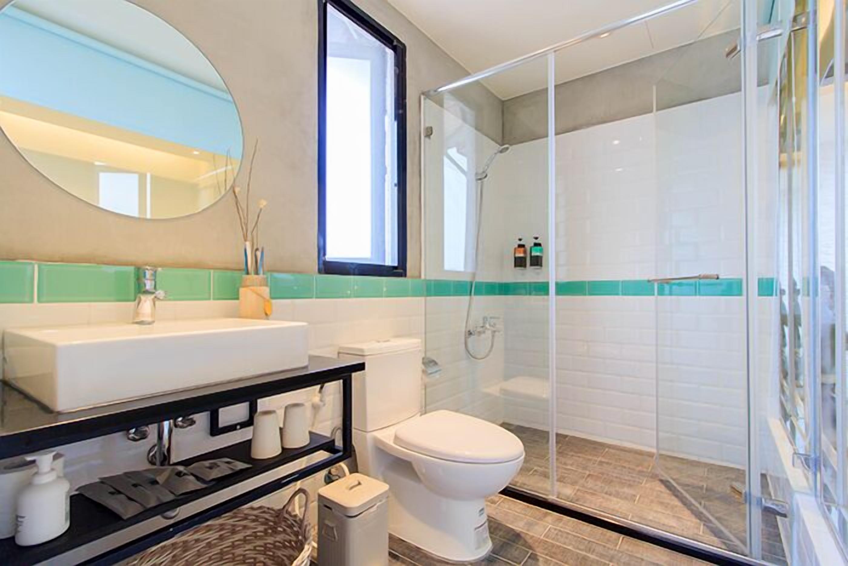 Un baño moderno con ducha de vidrio, inodoro blanco y lavamanos con espejo.
