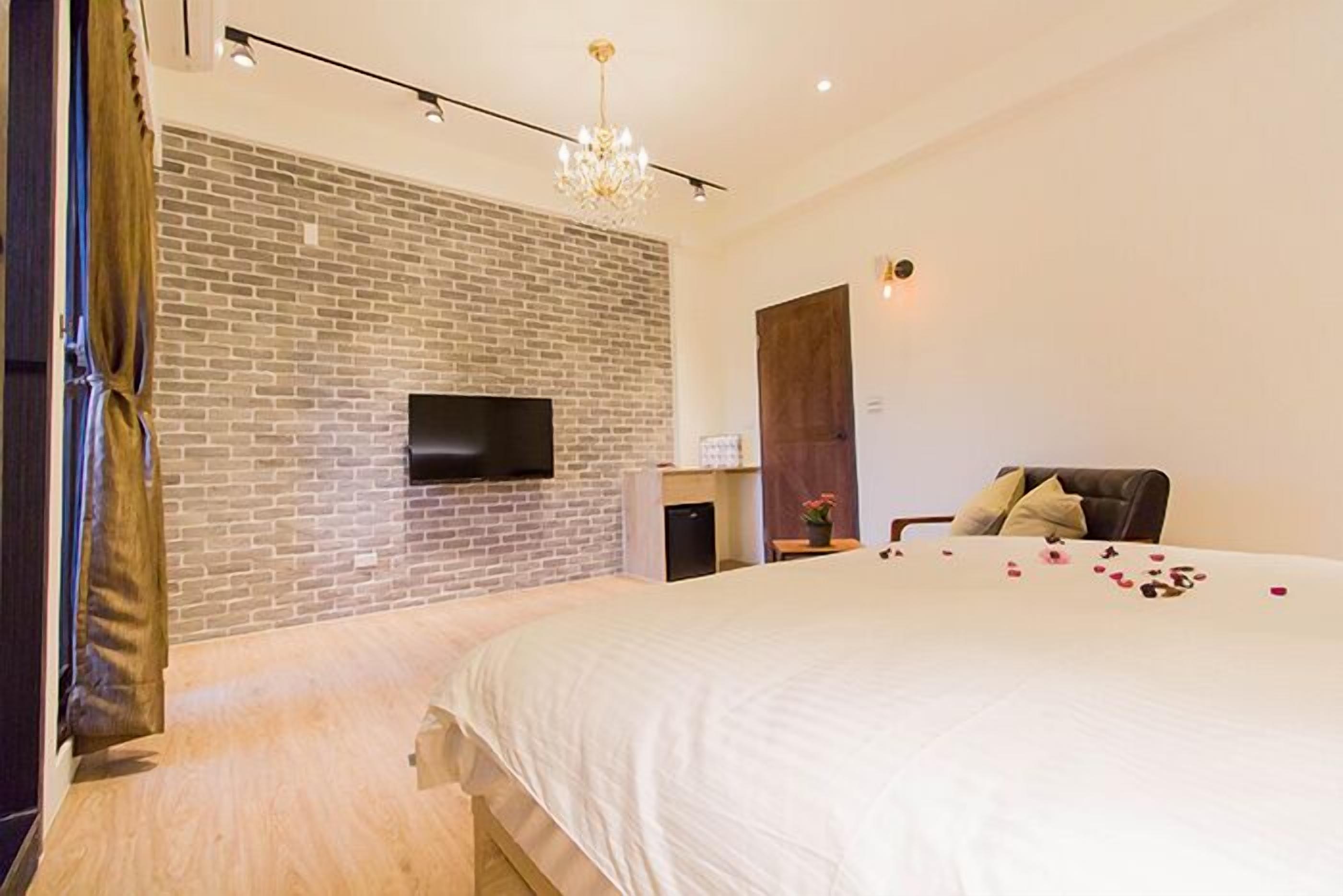 A modern bedroom with a brick wall, a flat-screen TV, a bed with rose petals, and a chandelier.