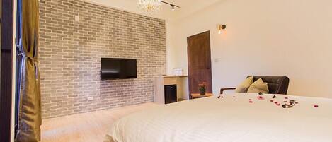 A modern bedroom with a brick wall, a flat-screen TV, a bed with rose petals, and a chandelier.