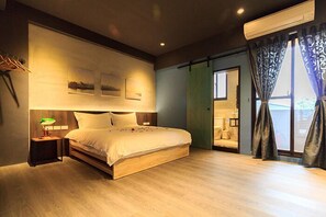 Un dormitorio con una cama grande, una mesita de noche con lámpara, un estante en la pared con fotografías y una puerta corredera que da a otra habitación.