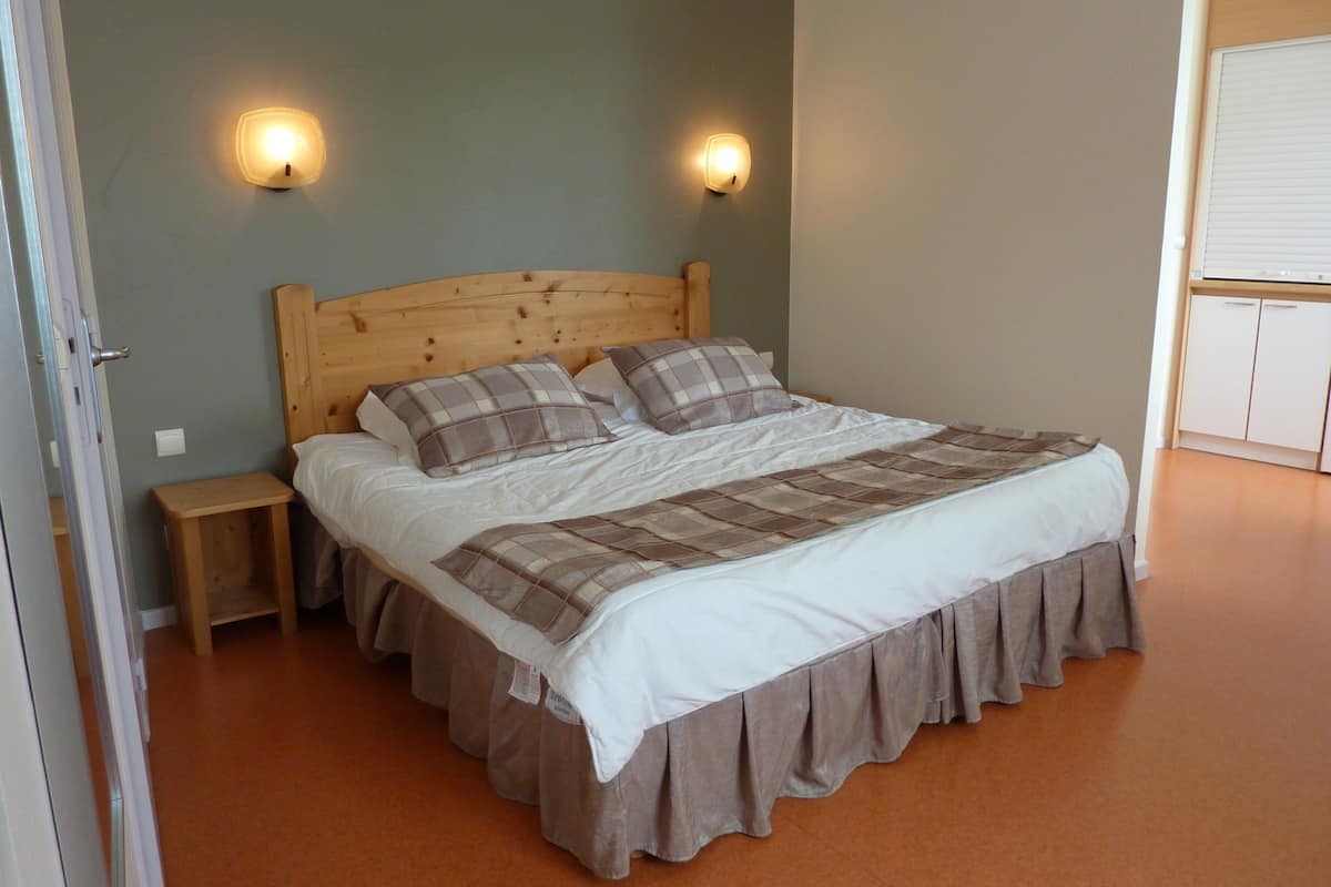 Een slaapkamer met een houten hoofdbord, twee nachtkastjes, een bed met een geruite plaid en twee wandlampen.