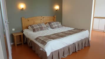 A bedroom with a wooden headboard, two bedside tables, a bed with a plaid bedspread, and two wall-mounted lights.