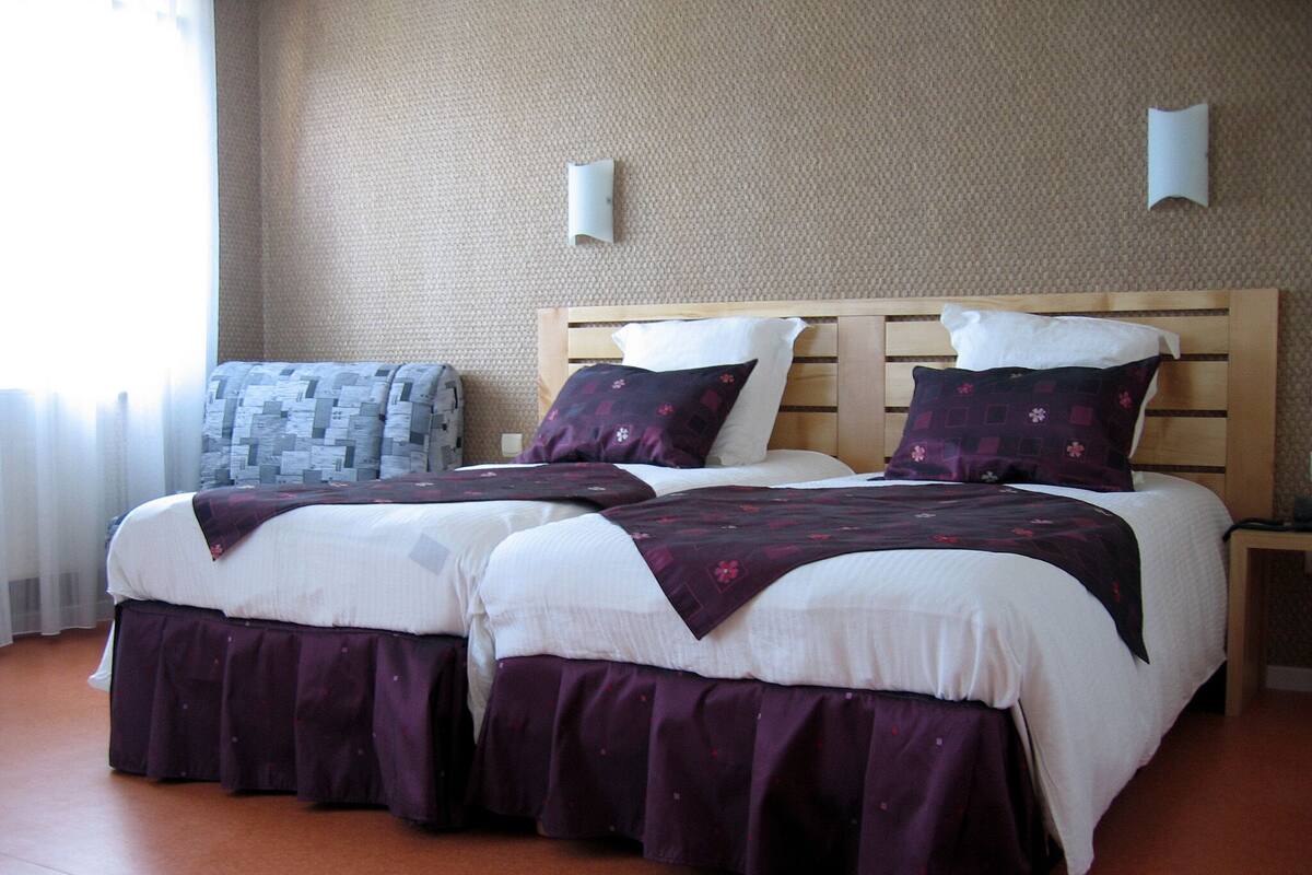 Een tweepersoonsbed met een houten hoofdbord, twee nachtkastjes en een geborduurde plaid.
