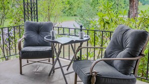 A balcony with two grey upholstered chairs and a small round table with two cups.
