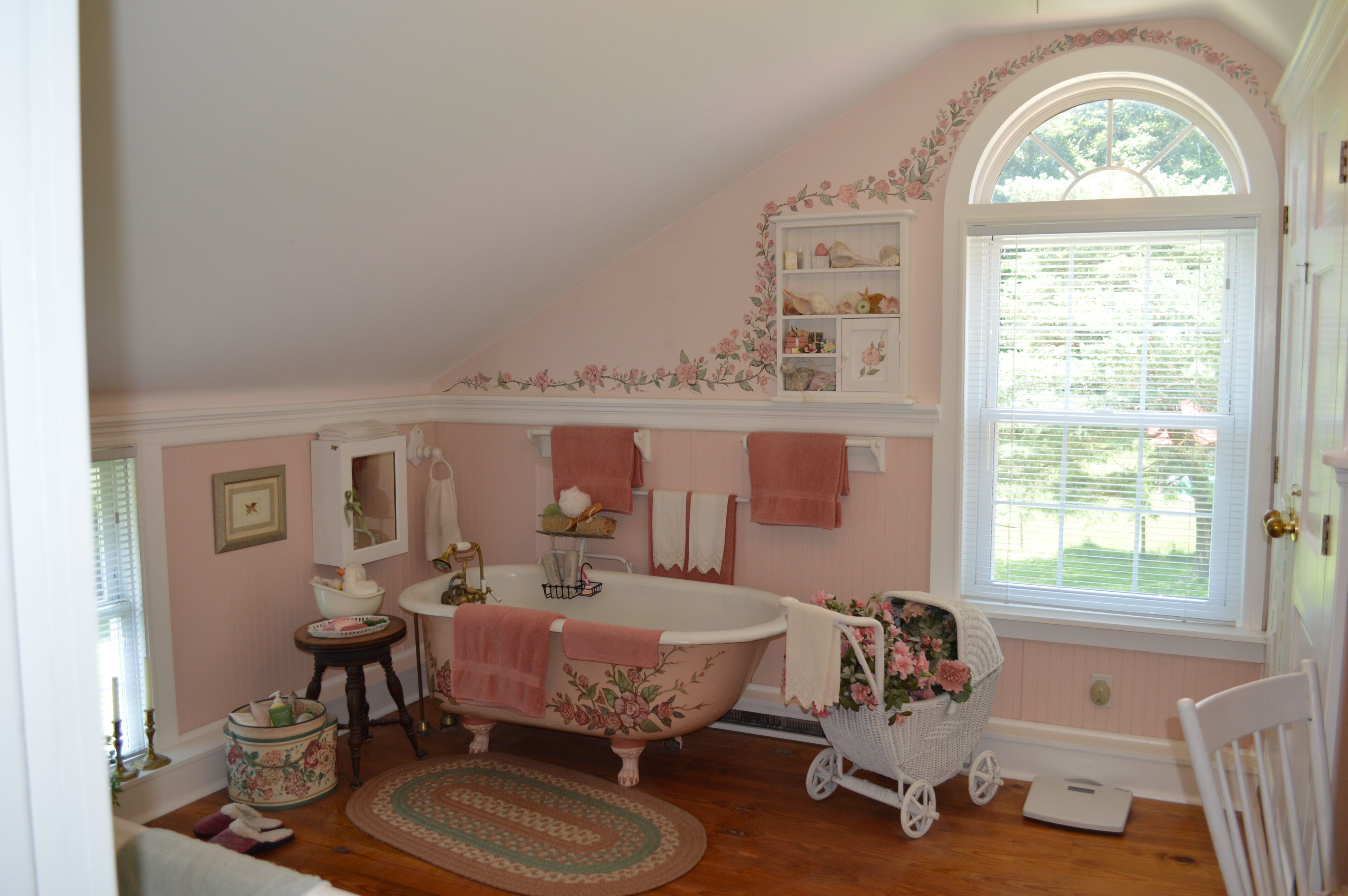 A bathroom with a clawfoot bathtub, a vanity with a mirror, a window with blinds, and a floral wall decoration.