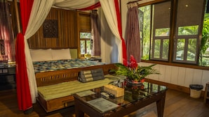 Una habitación con una cama, una mesa de vidrio y vista a la vegetación exterior.