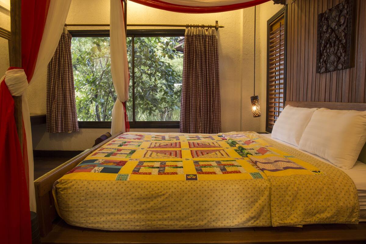 A bed with a quilt, a window with curtains, and a wall-mounted light fixture.