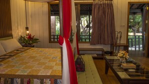 Una habitación con cama, un banco, una mesa con un florero y una ventana con cortinas.