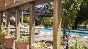 Una terraza de madera con macetas de terracota y una piscina al fondo.