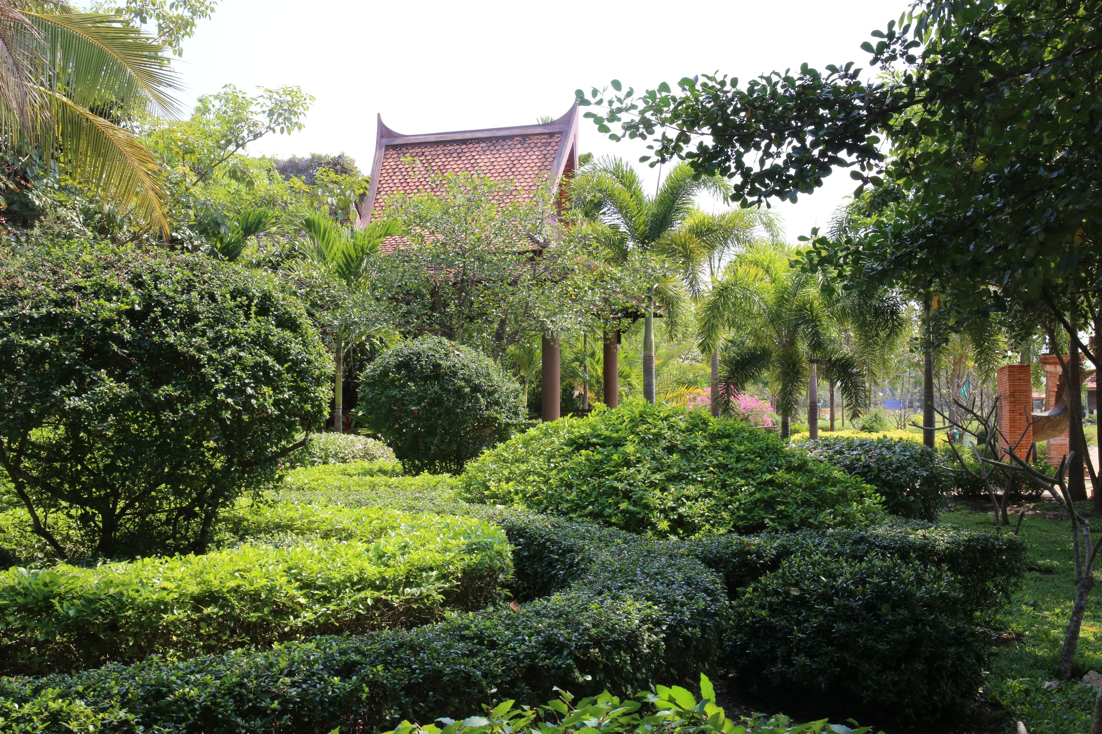 A traditional building with a tiled roof, surrounded by well-maintained greenery and palm trees.