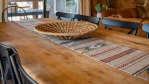 Une table à manger en bois, des chaises, un set de table en fibres tressées et un luminaire suspendu.