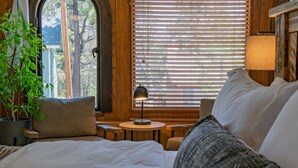 Une chambre à coucher avec un grand lit, une table de chevet, une lampe, une plante en pot et une fenêtre avec des stores.