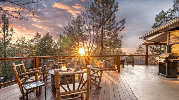Une terrasse en bois avec un foyer et du mobilier d’extérieur, donnant sur une zone boisée.