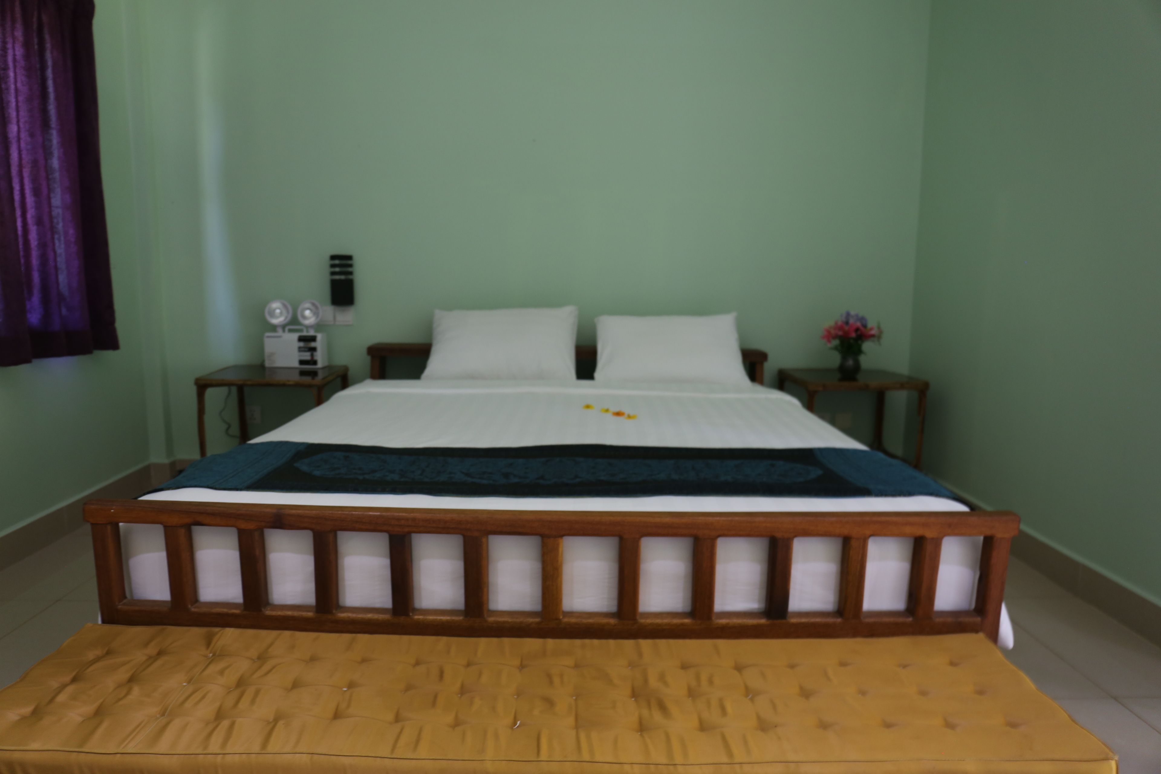 A bedroom with a large bed, two bedside tables, a nightstand, and a small table with flowers.