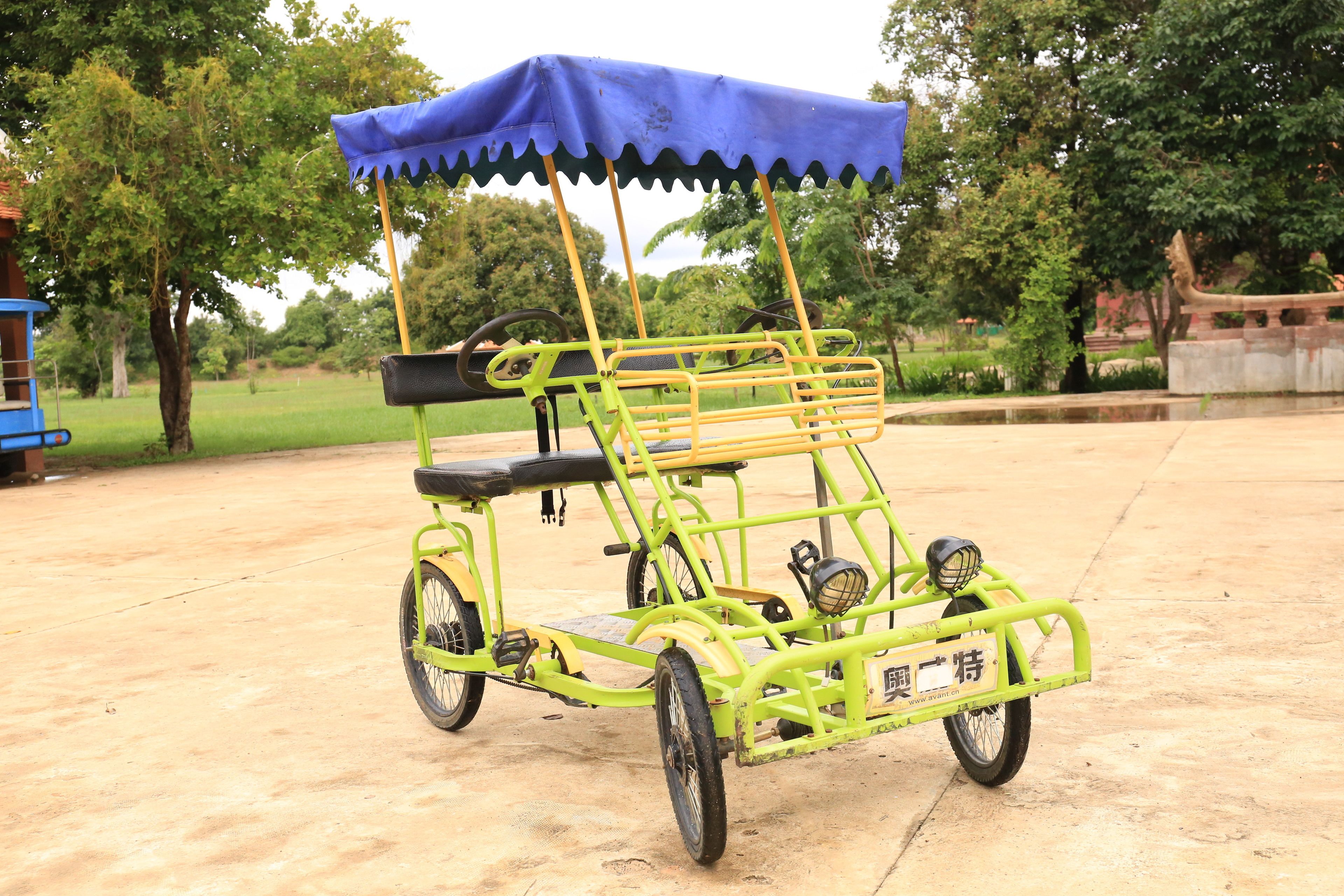 A green and yellow rickshaw with a blue canopy parked on a concrete surface.