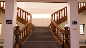 A staircase with wooden balusters and a handrail, flanked by two columns with directional signs. - Samrith Hotel (Baray)