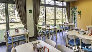 Un comedor con mesas y sillas, ventanas amplias con cortinas y vistas al exterior.