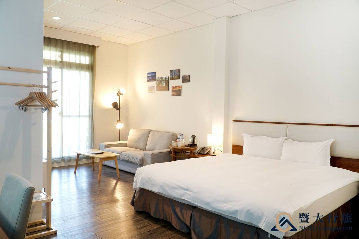 A hotel room with a large bed, a sofa, a desk, and a wardrobe.