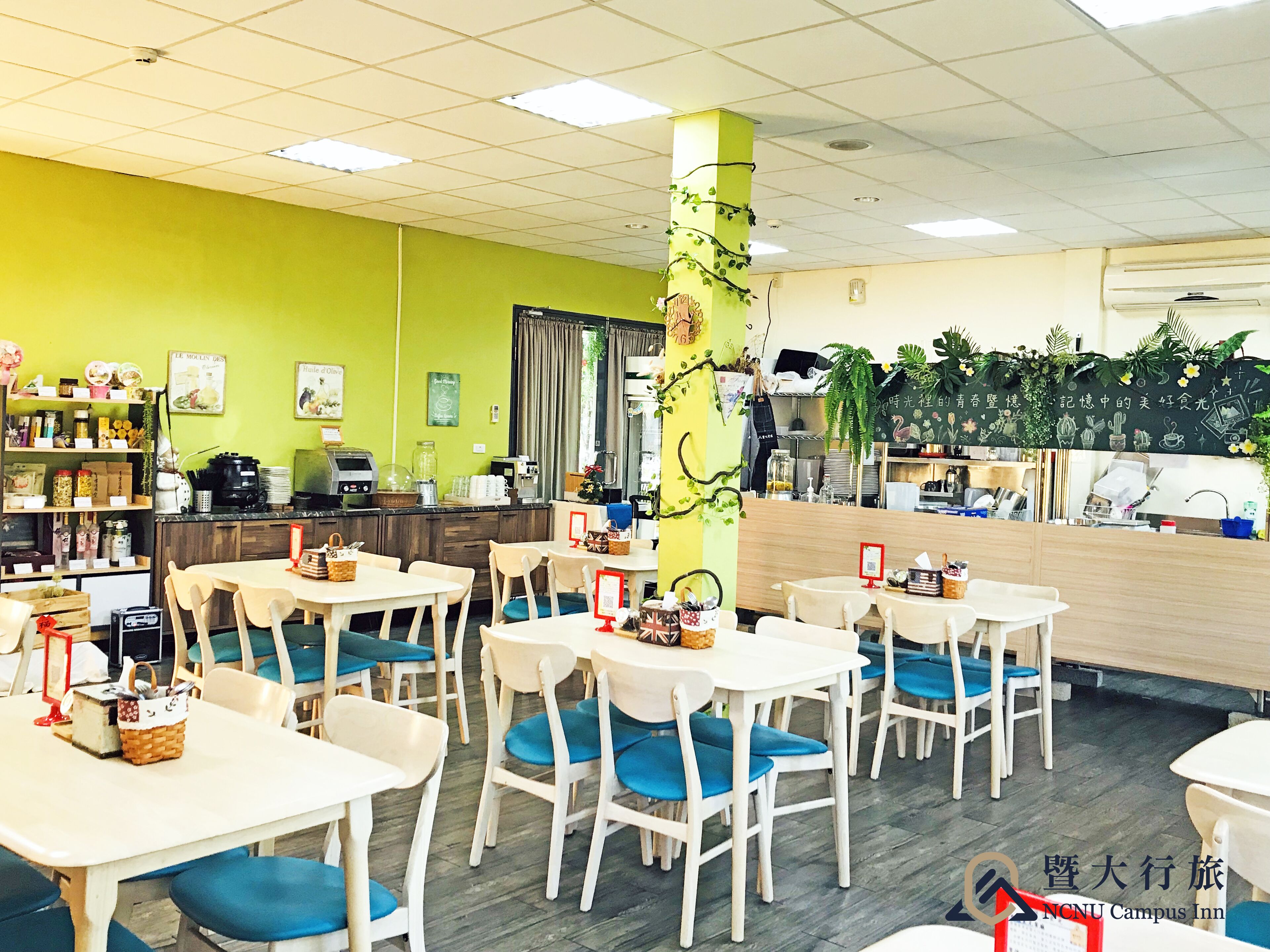 A dining area with tables and chairs, a counter with a coffee machine, and a green wall with decorations.