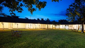 Un patio de hotel al anochecer con césped, mobiliario exterior e iluminaciones en las ventanas.