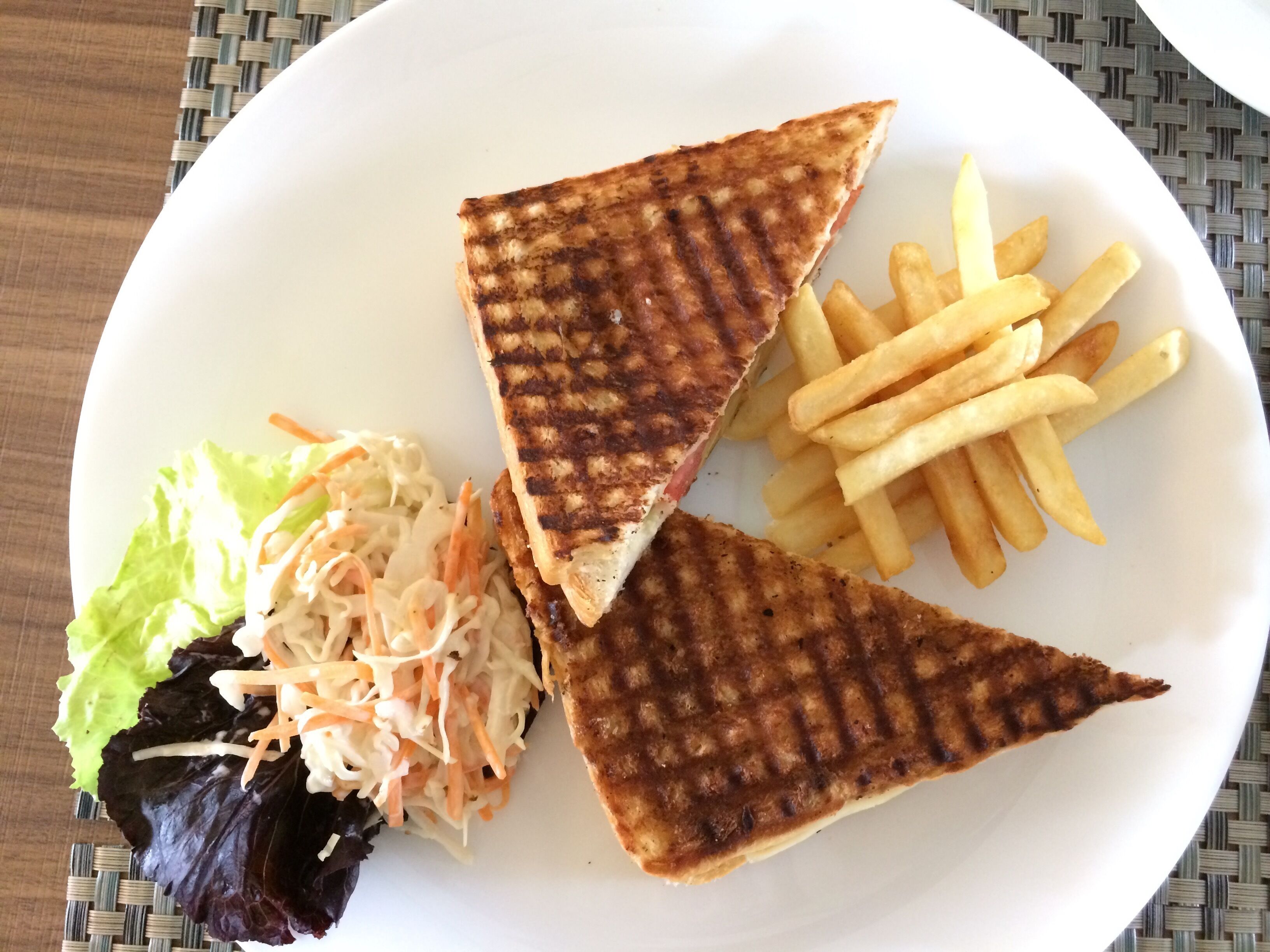 Une assiette avec des moitiés de sandwich grillé, des frites et une salade d’accompagnement.
