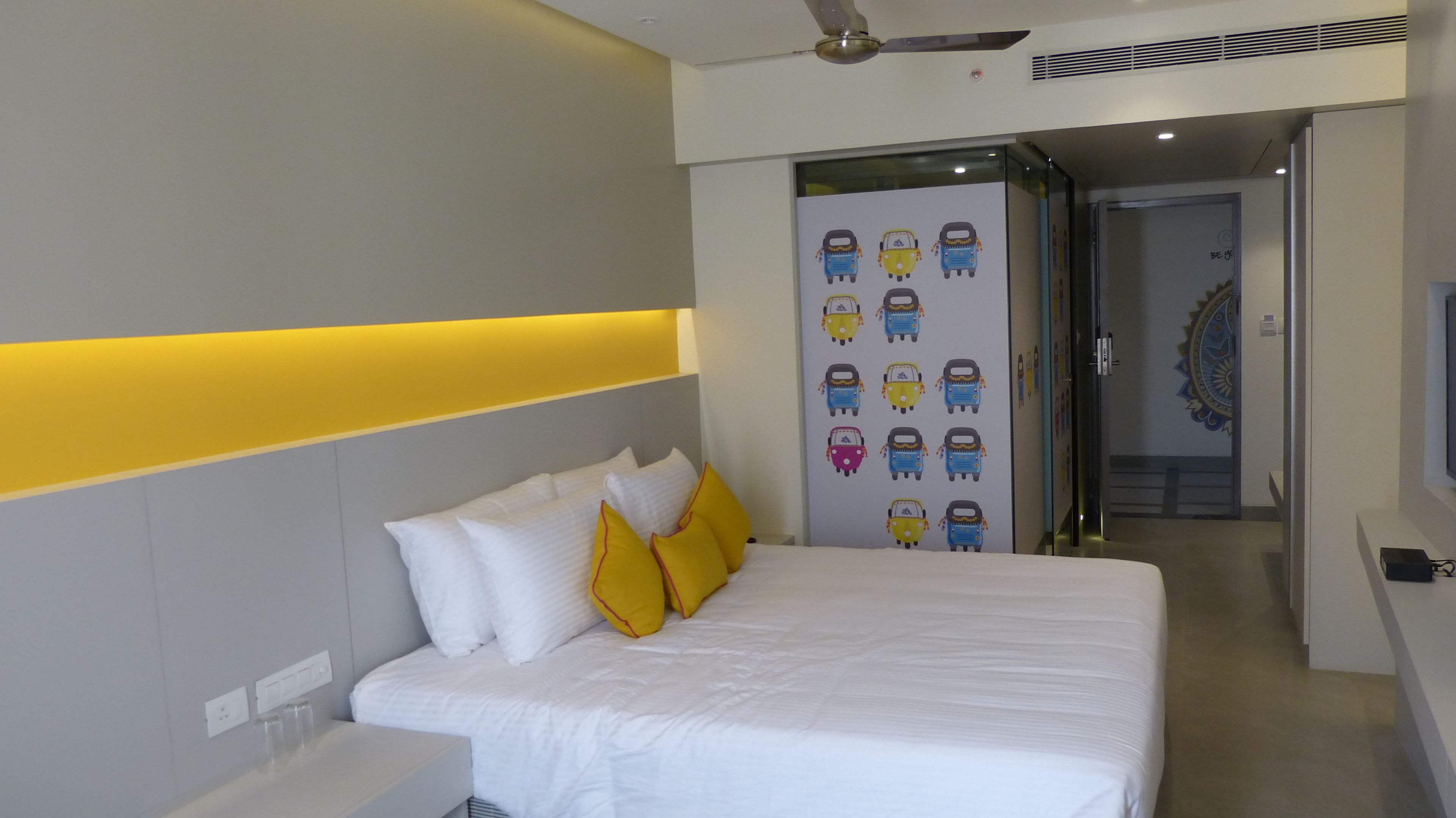 Une chambre d’hôtel moderne avec un lit bien fait, une table de chevet et un mur décoré d’un autocollant représentant un véhicule aux couleurs vives.