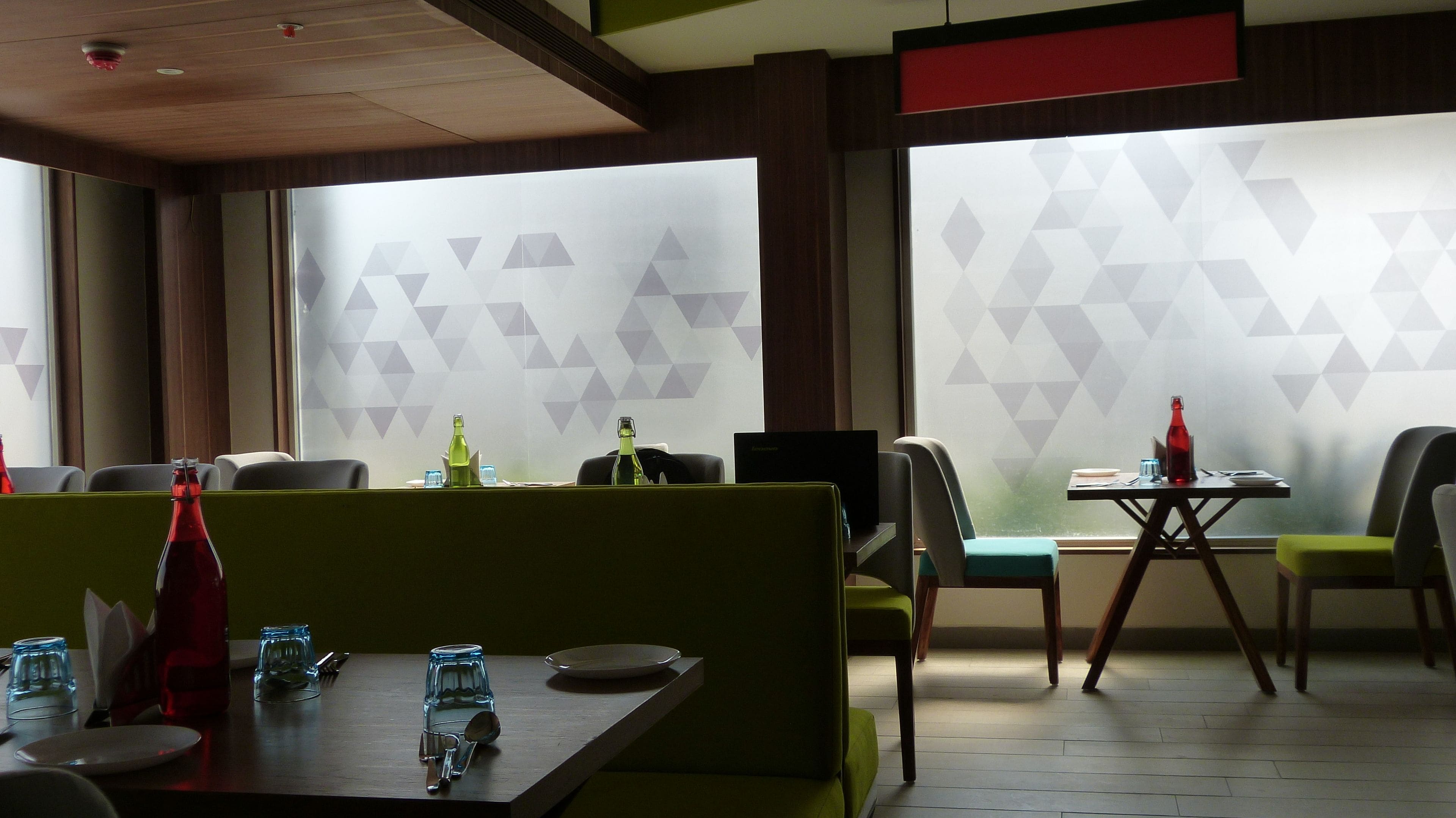 Ein Restaurant mit Sitzecken und Tischen, Wänden mit geometrischem Muster und Blick durch ein Fenster.