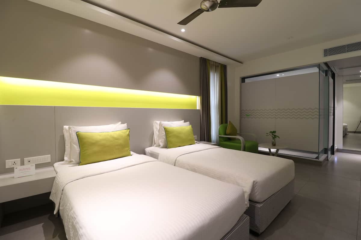 A modern hotel room with two beds, a ceiling fan, a bedside table, and a large sliding door leading to a balcony.