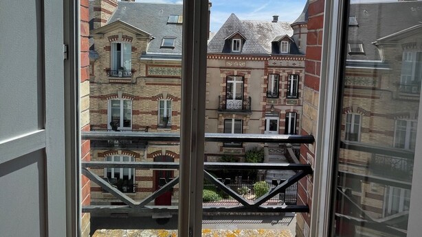 Blick aus einem Fenster mit Metallgitter auf eine Reihe mehrgeschossiger Gebäude mit Backsteinfassaden und zahlreichen Fenstern.